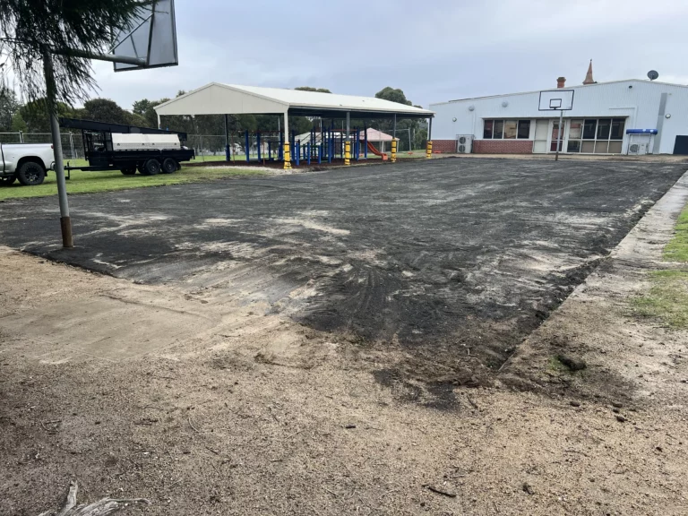 Black synthetic layer being installed over the prepared ground for a new sports court.